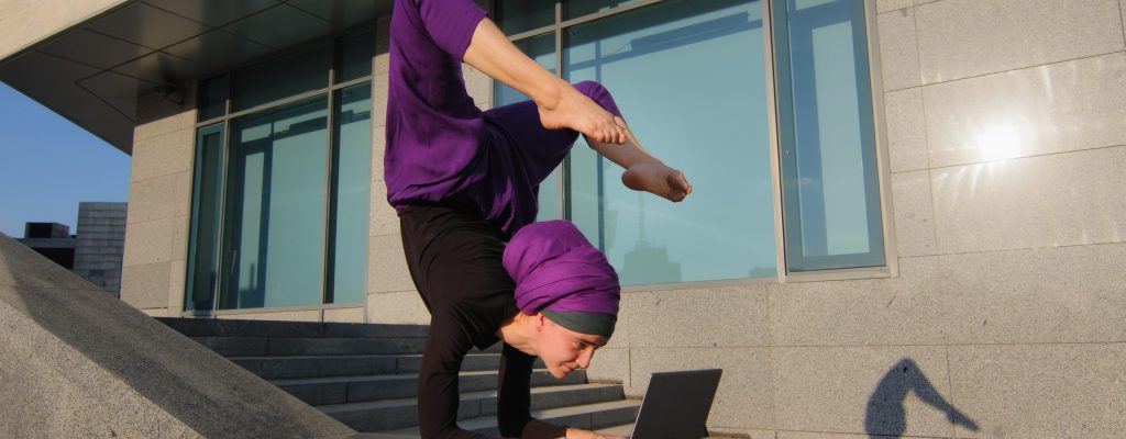 Strong acrobat business woman funny muslim girl in hijab stands on hands in acrobatic yoga pose asana balance handstand in city outdoors typing laptop working remotely online keep legs in air position. High quality 4k footage
